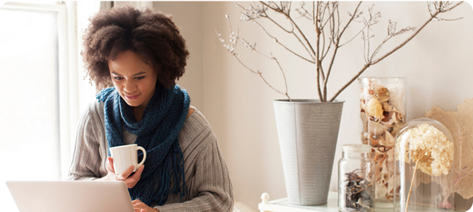 Person sits and looks at laptop while drinking coffee
