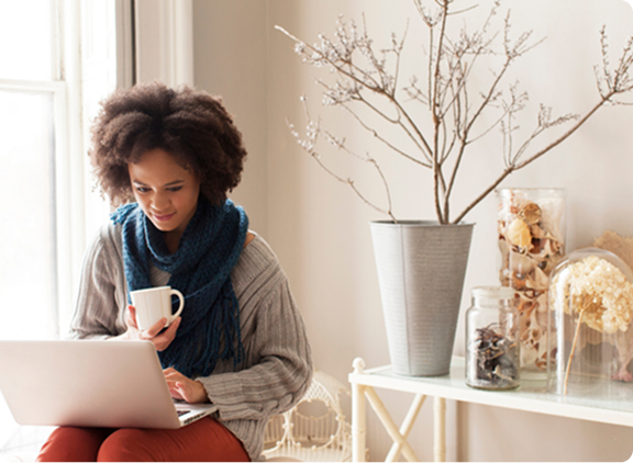 Person sits and looks at laptop while drinking coffee
