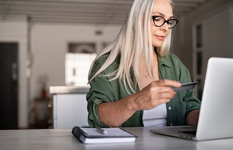 Person sits and looks at laptop with Card in hand