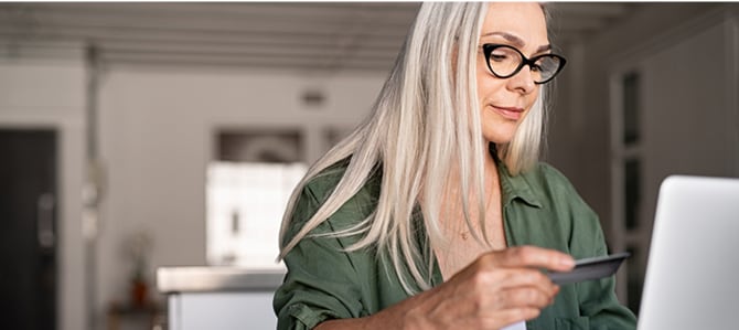 Person sits and looks at laptop with Card in hand