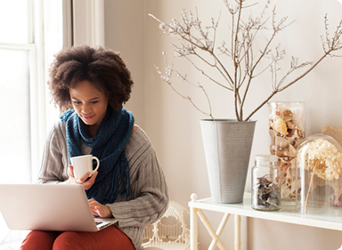 Person sits and looks at laptop while drinking coffee