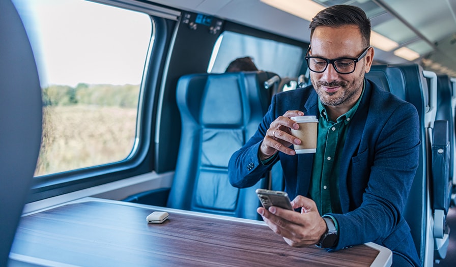 Man sitting on the train with coffee and looking at his phone