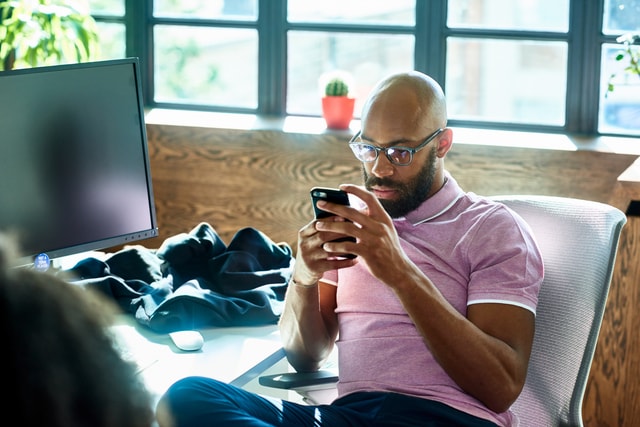 Man sitting at desk, checking smartphone, reading messages.