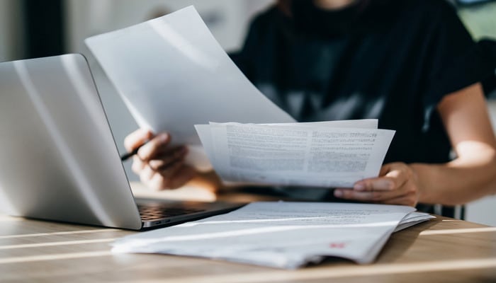 A woman at a library studying with some notebooks and a laptop.