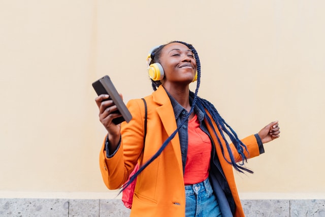 Woman with headphones and smart phone dancing outdoors.
