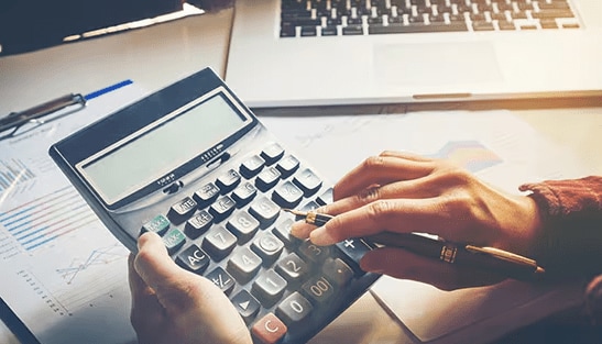 A person using a calculator near a laptop