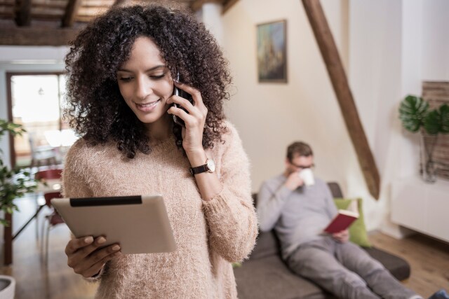 Una mujer hablando por teléfono y mirando su tableta en casa.