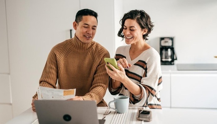 A couple in their kitchen looking at a mobile phone.