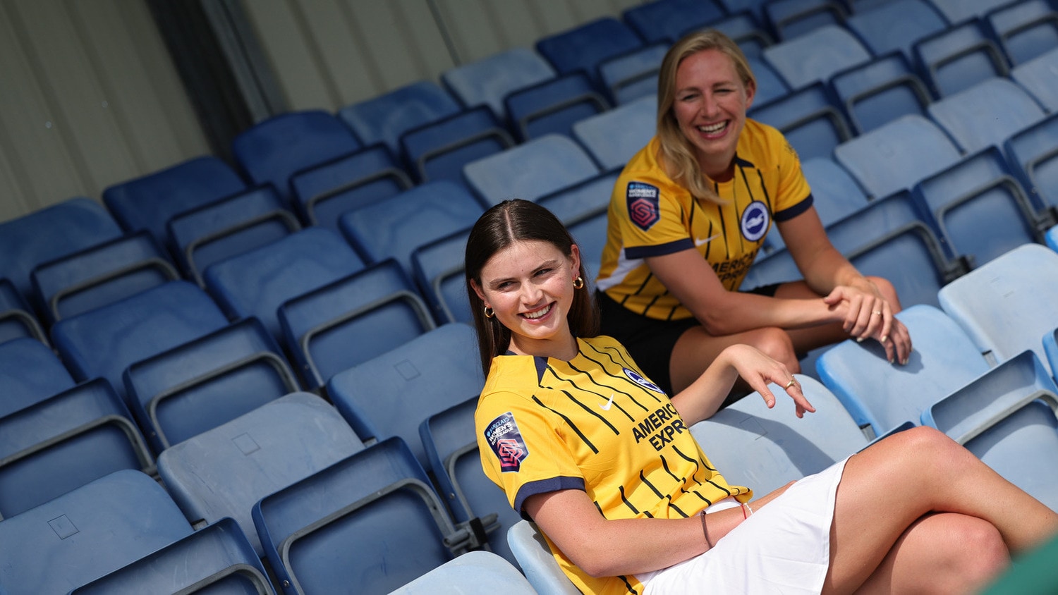 Two Brighton & Hove Albion players sitting in the stands wearing the away kit.