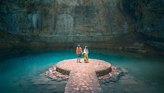 Two people holding hands inside a zenote cave lake in Mexico