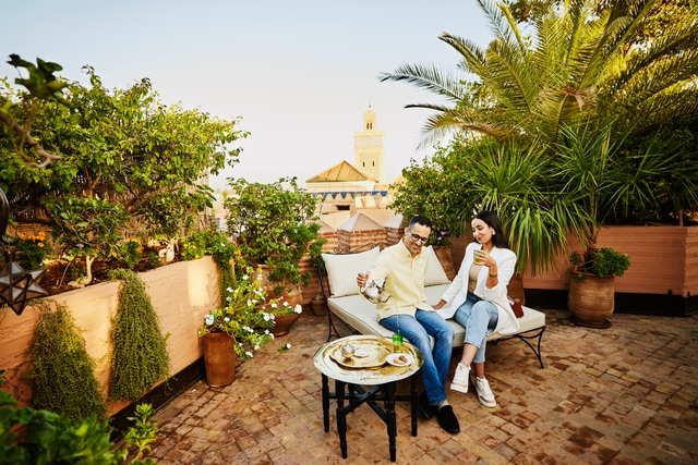 Smiling couple having tea on rooftop deck of luxury hotel overlooking the Medina of Marrakech.