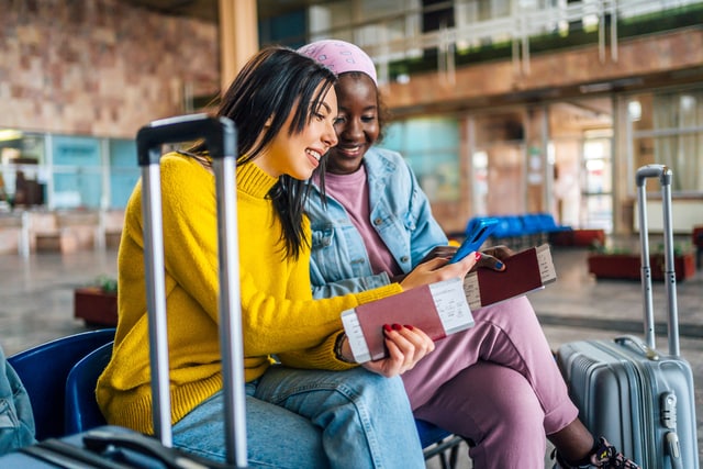 Friends looking at mobile phone at the airport while waiting for their flight