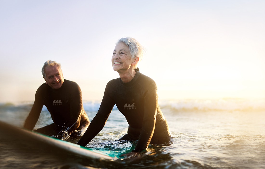 A couple in wetsuits sitting on surfboards in the sea