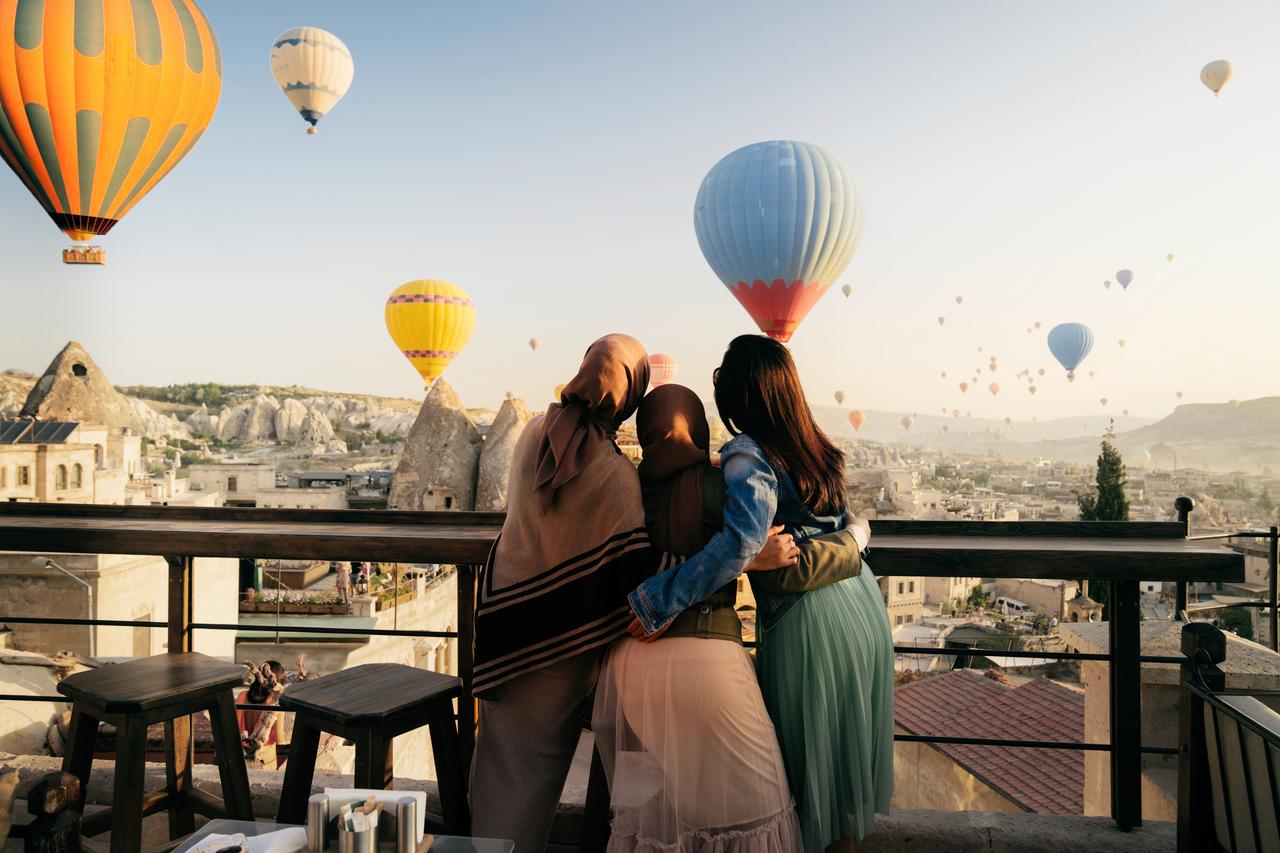 three women watching hot air balloons on a terrace