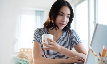 Woman holding coffee mug and looking at laptop