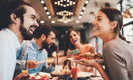 Four people in a restaurant sitting at a table laughing and eating food 