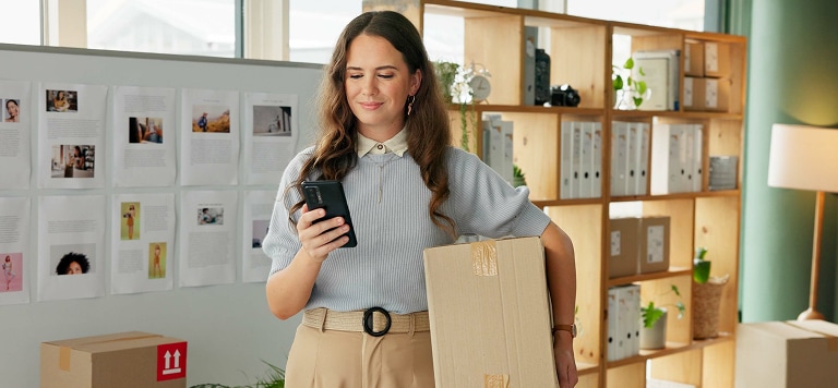 Woman in office holding box and phone                 