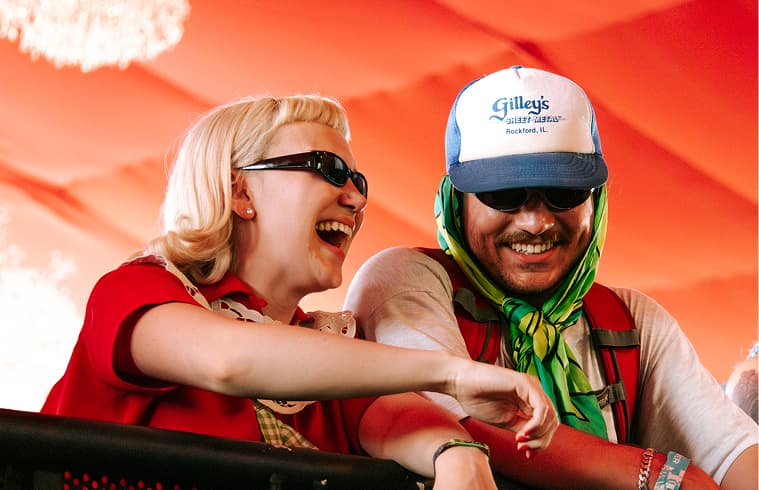 Two colorfully dressed festival attendees smile while leaning on a counter.