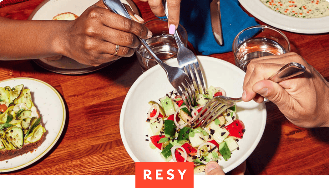People sharing a salad and small plates at a restaurant table. Resy