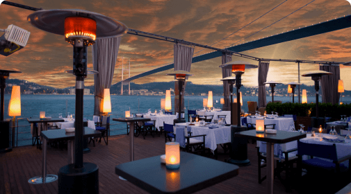 Tables looking out on the water with lights and heaters showing a By Invitation Only event