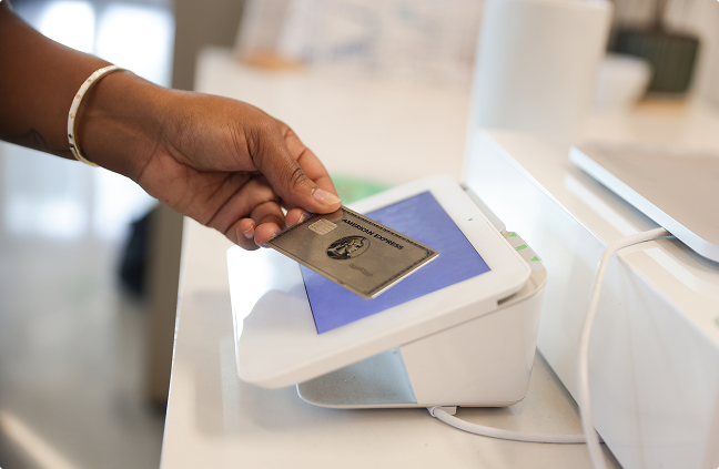 Hand tapping an American Express Platinum Card against a card reader screen