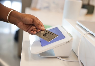 Hand tapping an American Express Platinum Card against a card reader screen