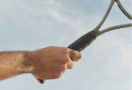 Close shot of a hand wearing an Oura ring holding a tennis racket