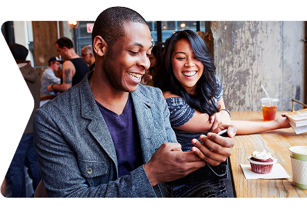 Two people looking at a device while enjoying a drink and dessert