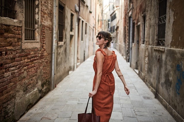 Woman in orange dress and sunglasses carrying an bag and looking back