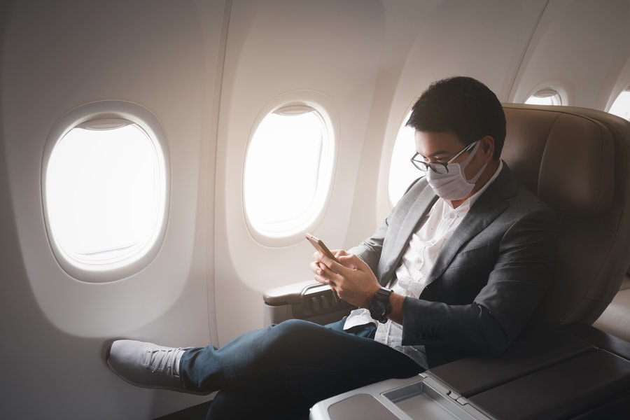  Man on airplane wearing mask, looking at phone
