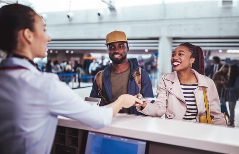 A couple collects their boarding passes from an agent at an airport.