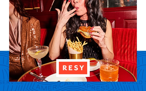 A woman licks her fingers and holds a burger in a restaurant.