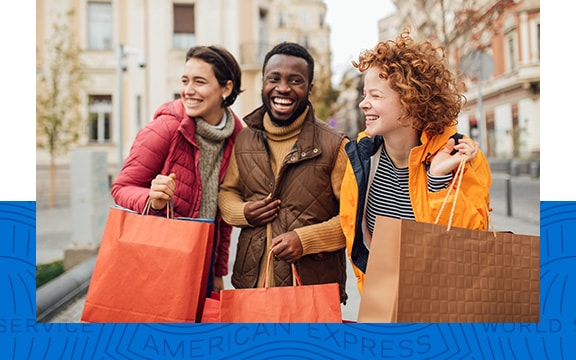 Three friends smile in a street holding shopping bags.