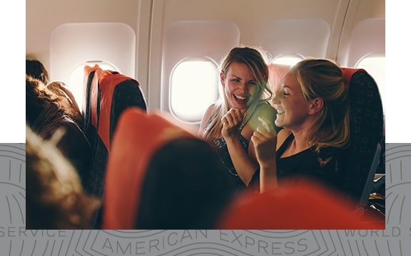 Two women laughing in their seats on a flight.