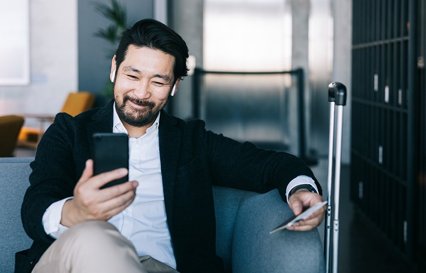 A man sitting at an airport, smiling at his phone.
