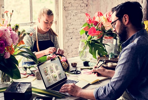 Man and Woman working in flower store while man looks at details on computer.