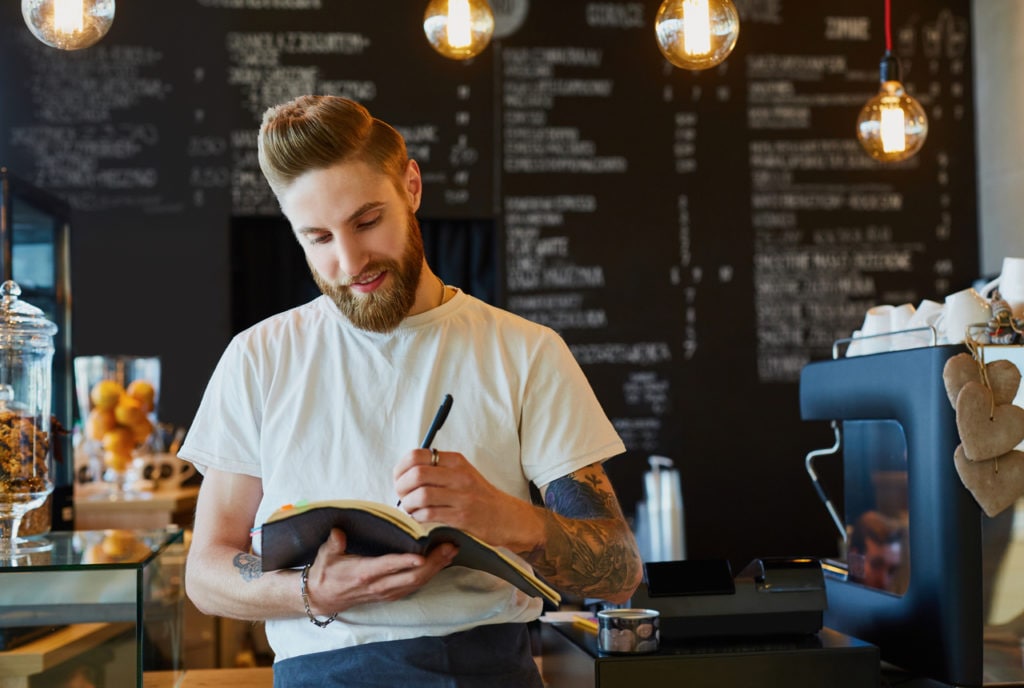 Man writing notes down in notebook in coffee shop.