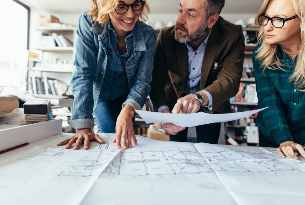 Two women and man looking at blueprints for a building.