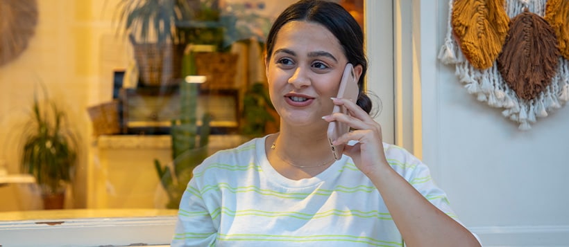 A woman sits in her kitchen drinking coffee while talking on her phone