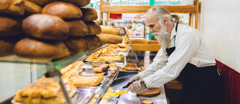 A baker cuts a piece of pie to serve to a customer