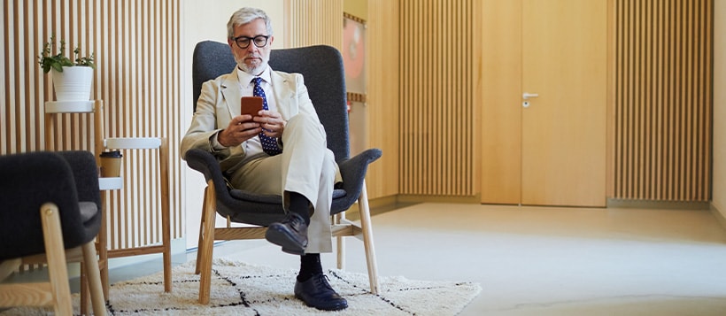 Business man checks his phone while sitting in an office lobby