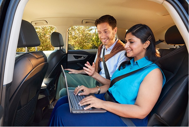 Woman typing on a laptop from backseat of a car next to a colleague.