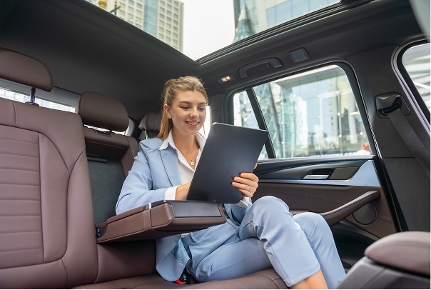 Woman viewing a tablet from the backseat of a car.