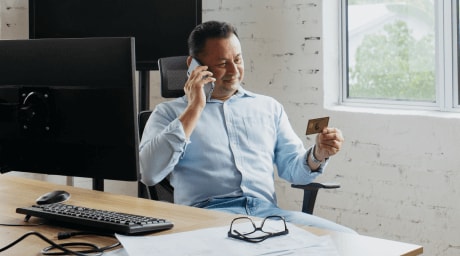 Man sitting at desk on cell phone holding American Express Card in his hand