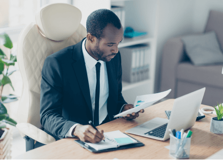Man sitting at desk working on laptop and writing in planner