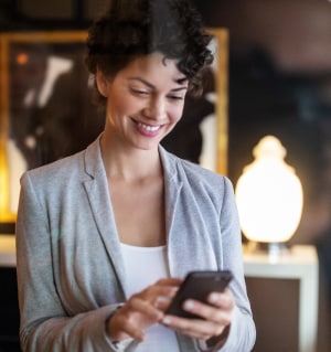 A businesswoman smiles down at her phone from the lobby of a hotel