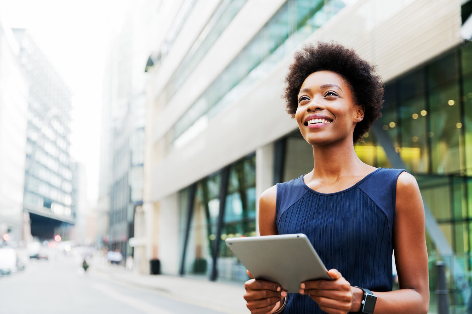 A businesswoman stands triumphantly outside an office building holding her tablet.