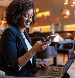 A businesswoman smiles down at her phone as she multitasks with her laptop.