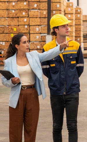 A businesswoman points something out to a man in a hard hat and reflective gear.
