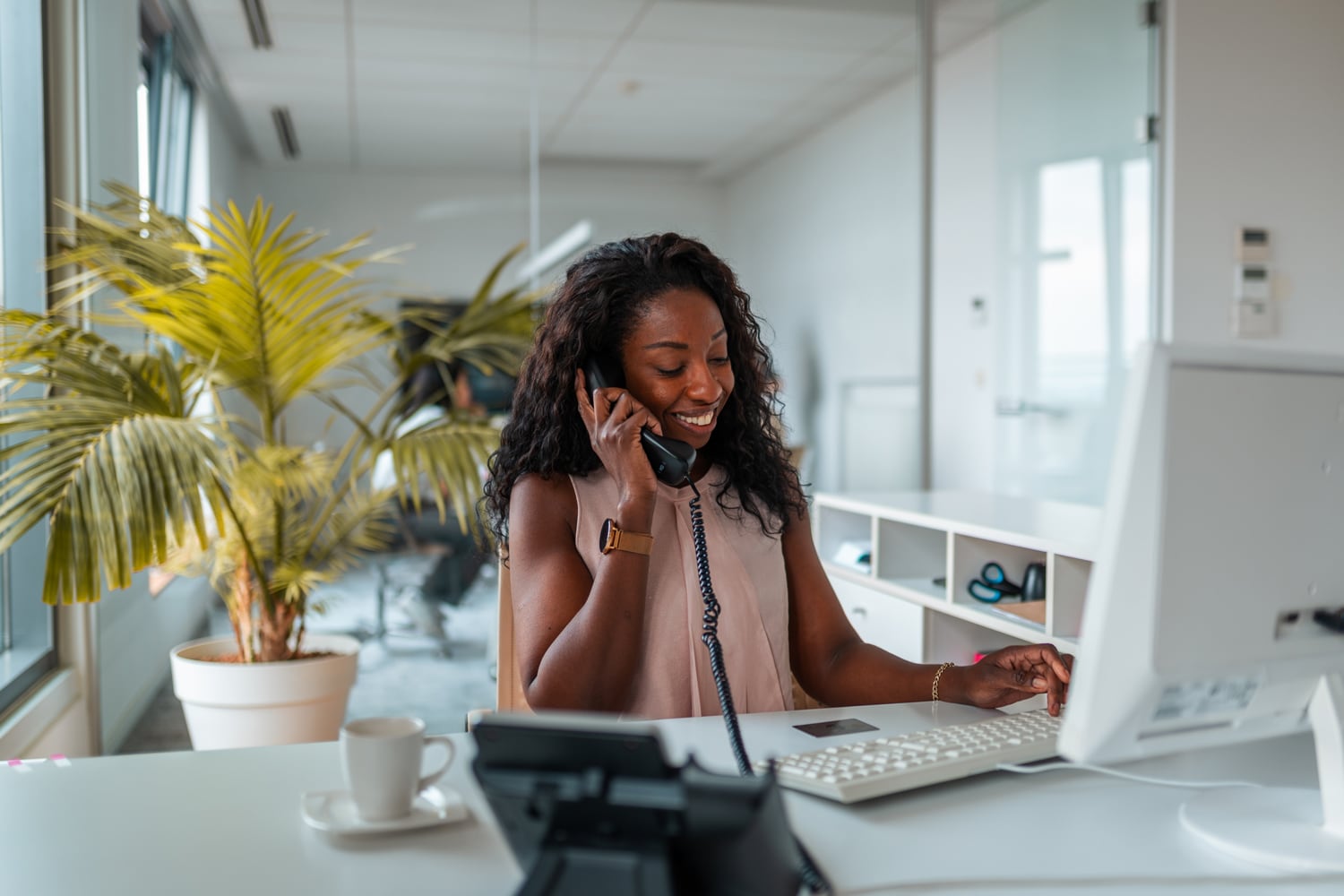 A businesswoman smiles as she balances talking on the phone and referring to her credit card.